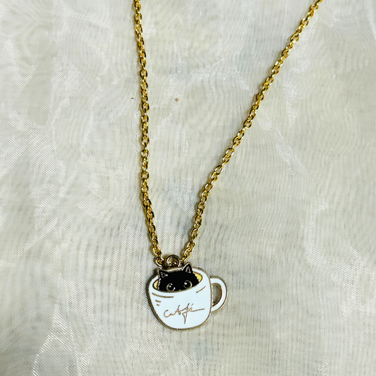 A gold-colored metal enamel charm depicting a black cat inside a white cup, attached to a golden chain, with a small gold chain attached to the top.
